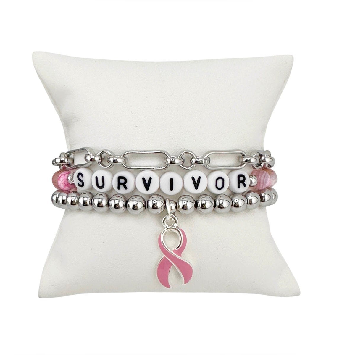 Love Lisa Survivor Breast Cancer Awareness Bracelet Stack in silver displayed on white pillow with SURVIVOR bead detail and pink ribbon charm