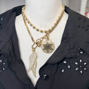 Gold necklace with star of david medallion layered with a necklace with angel wing charms on a mannequin bust wearing a black shirt.