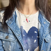Woman wearing a 16-inch gold chain necklace with a red enamel Italian horn charm, styled with a denim jacket and heart-printed shirt.