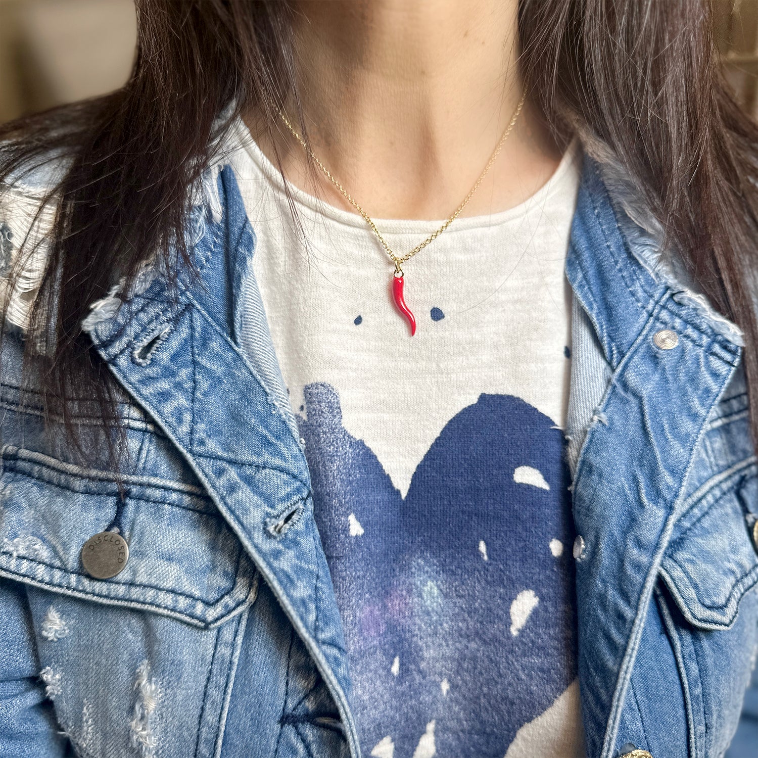 Woman wearing a 16-inch gold chain necklace with a red enamel Italian horn charm, styled with a denim jacket and heart-printed shirt.