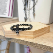 Black beaded bracelet with cross charm on a wooden stand