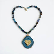 Necklace with blue and black beaded chain and a blue pendant with gold heart design on a white background