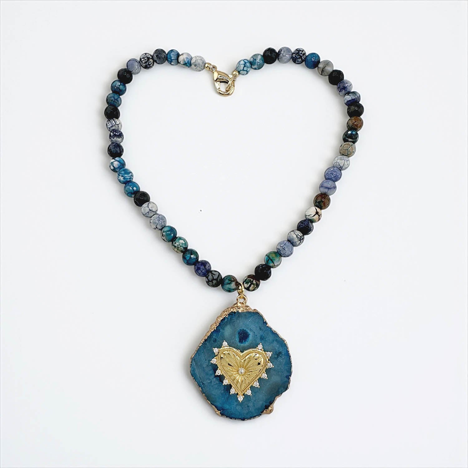 Necklace with blue and black beaded chain and a blue pendant with gold heart design on a white background