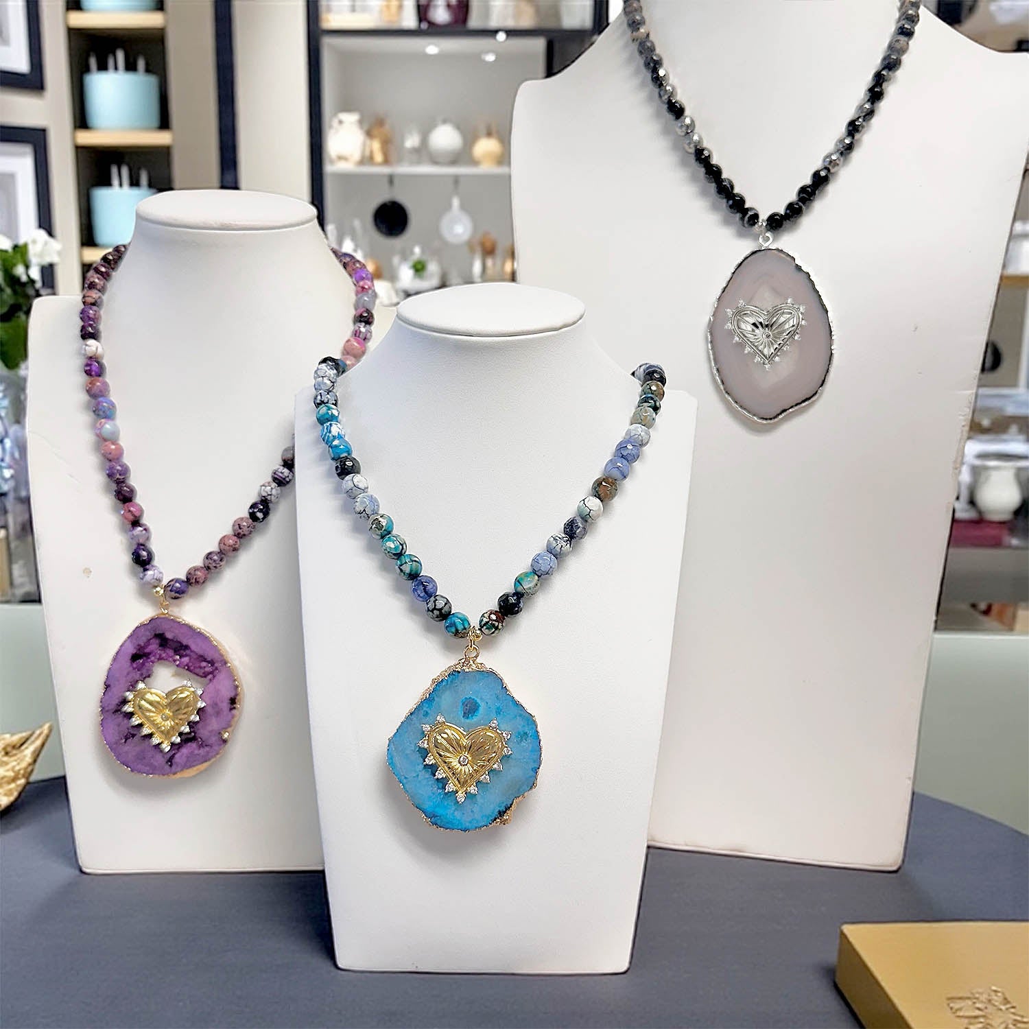 Three necklaces with heart-shaped pendants on white stands in a store setting.