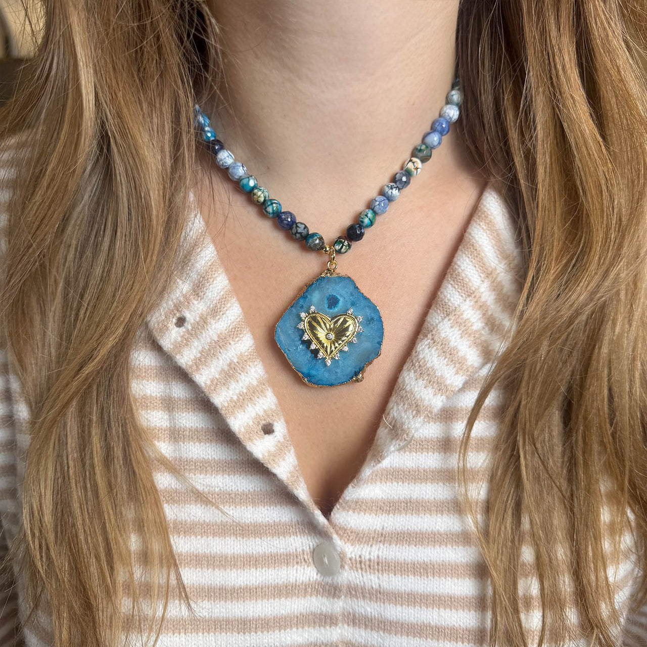 Necklace with a blue pendant featuring a heart design worn by a person with long hair.