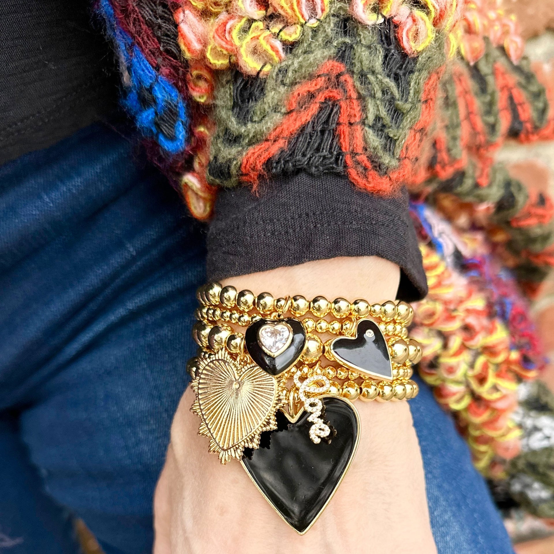 Black enamel heart bracelet stack worn on wrist with gold beaded heart charms