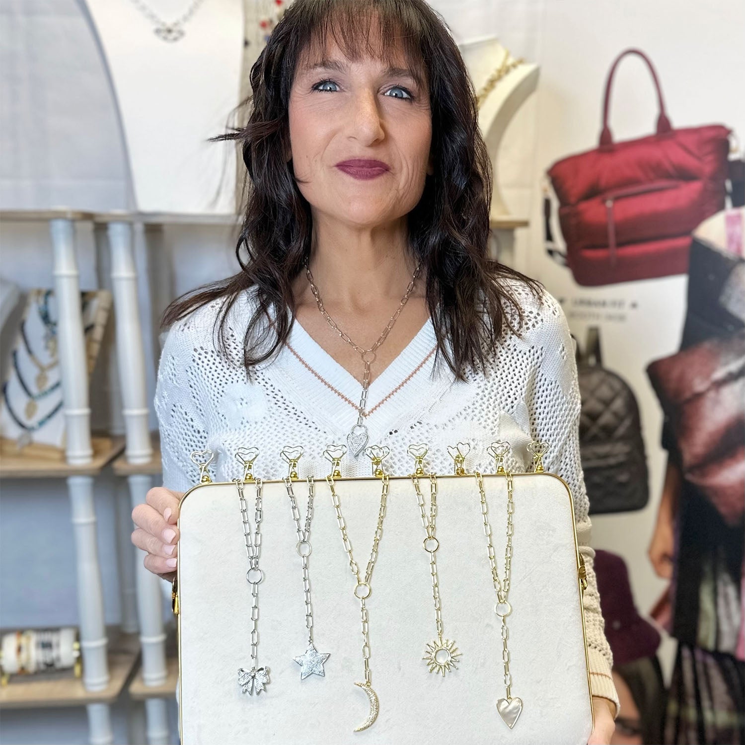 Woman holding a white clutch with hanging necklaces in a store setting