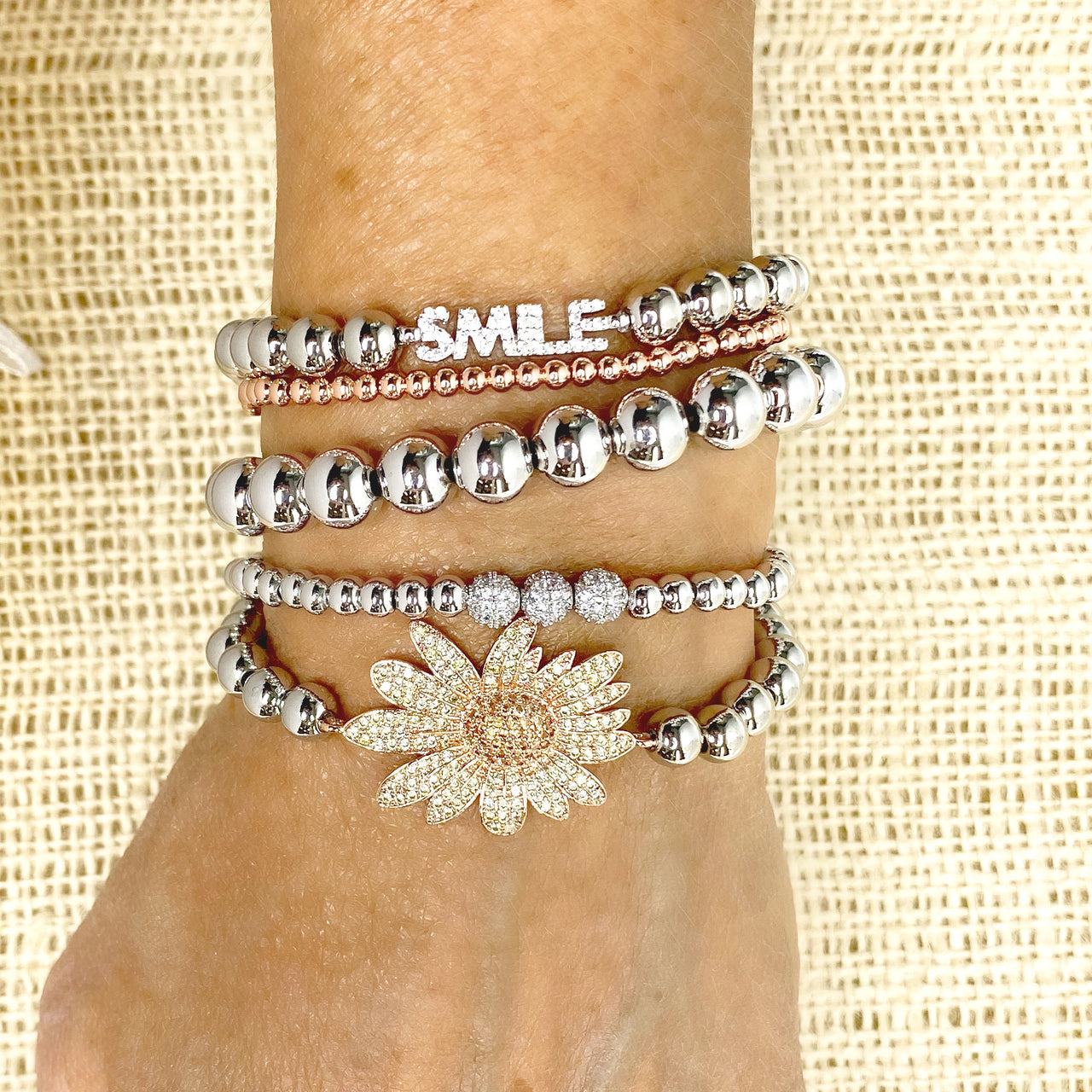 stack of mixed metal bracelets on wrist including gold sunflower charm bracelet with polished beads and floral pendant