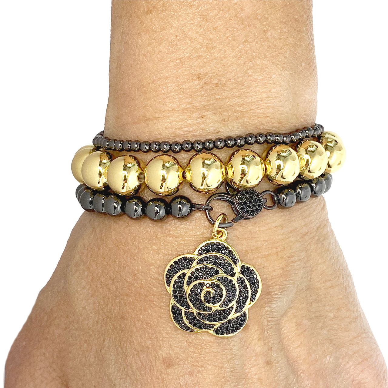 Beaded clasp bracelet styled with rose flower charm and stacked with beaded bracelets on wrist